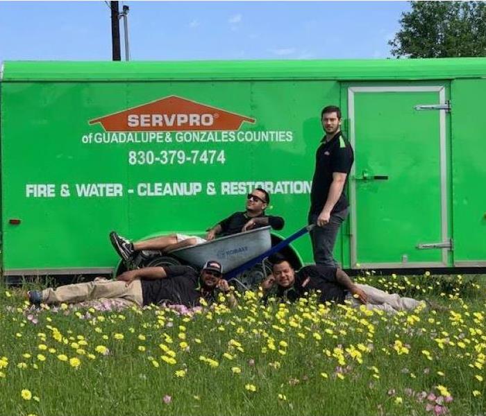 Our technicians in a field of flowers with one of them in a wheelbarrow. They are in front of a SERVPRO trailer