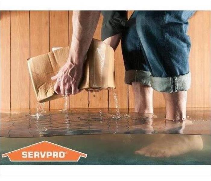 Someone standing a home with water up to their ankles is picking up a wet carboard box