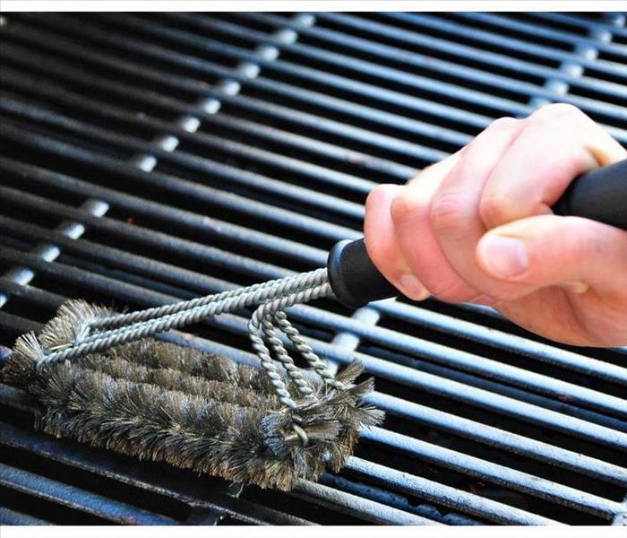 Hand with a brush cleaning a grill.