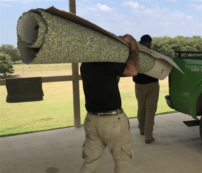 Technician carries rolled up carpet towards the truck to throw away.